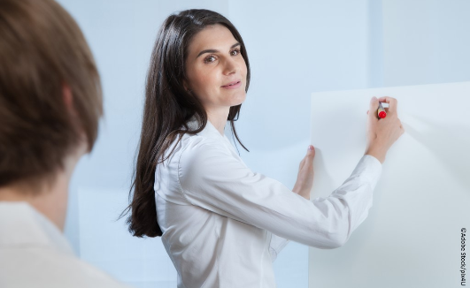 Referentin steht an einem Flipchart und blickt über die Schulter. Foto: Adobe Stock/pix4U